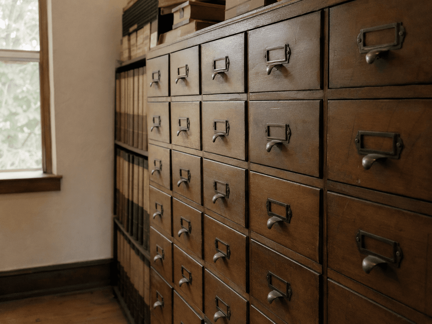 A wall of wooden record drawers with brass label holders in a records room.